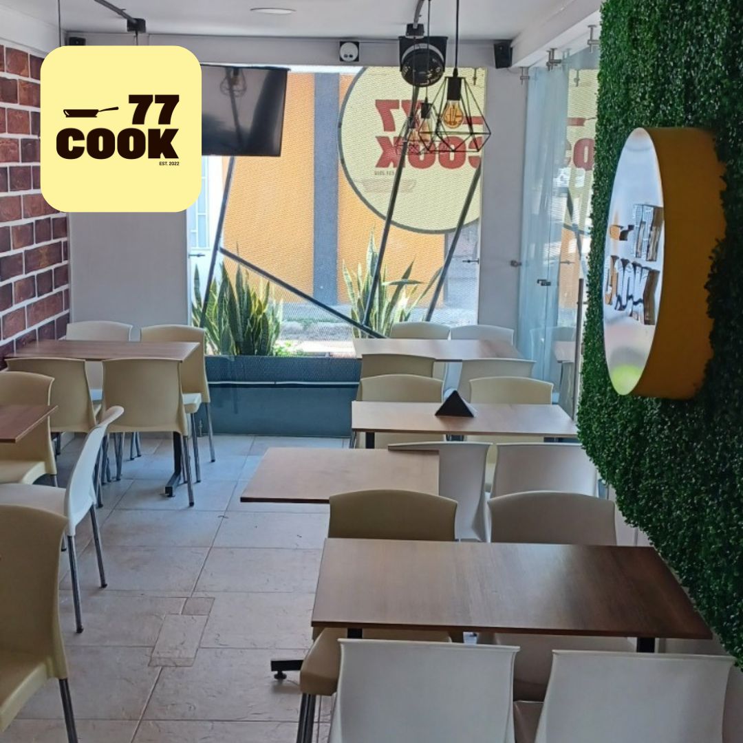 Restaurante con sillas y mesas color beige decoración de vegetación y letrero