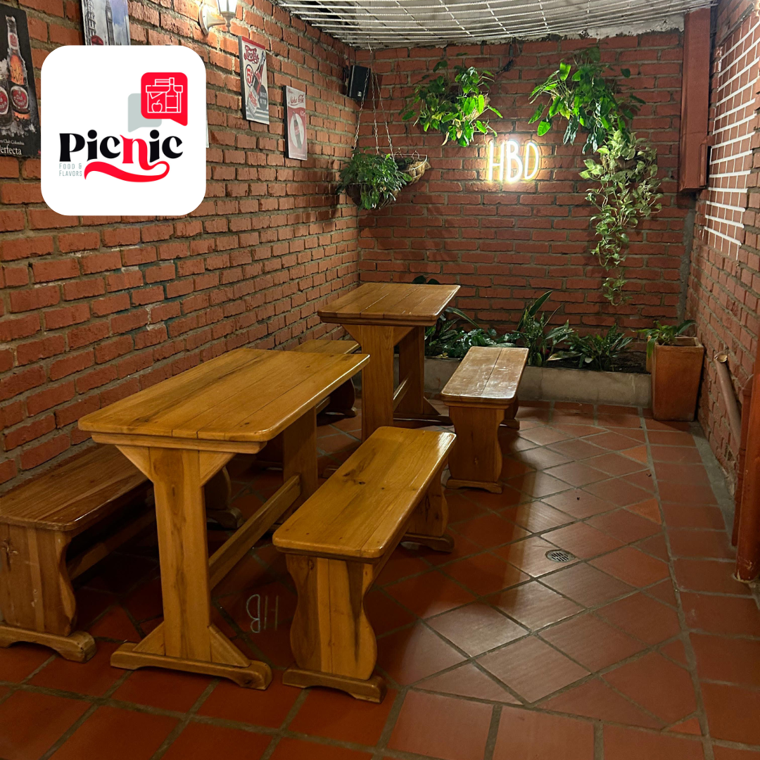 Imagen de restaurante con mesa y banco de madera con vegetación y letrero les de fondo