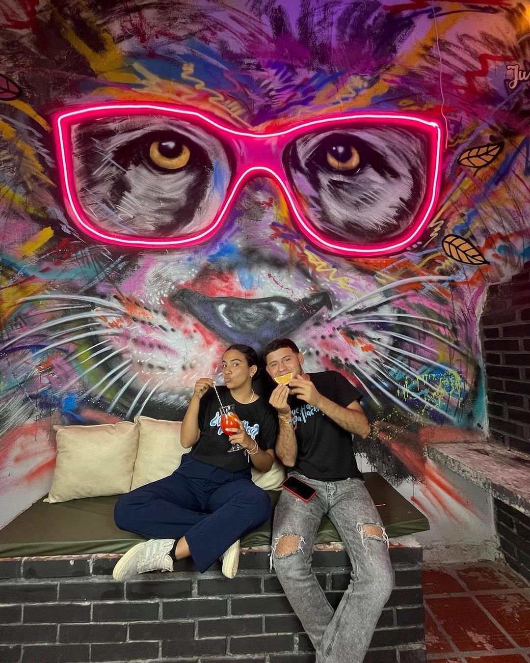 Gastrobar con pareja compartiendo coctel mural de perro en pared con gafas neón