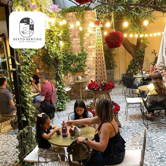 Restaurante con personas compartiendo mesas y sillas replica de torre Eiffel en la mitad vegetación y rosas