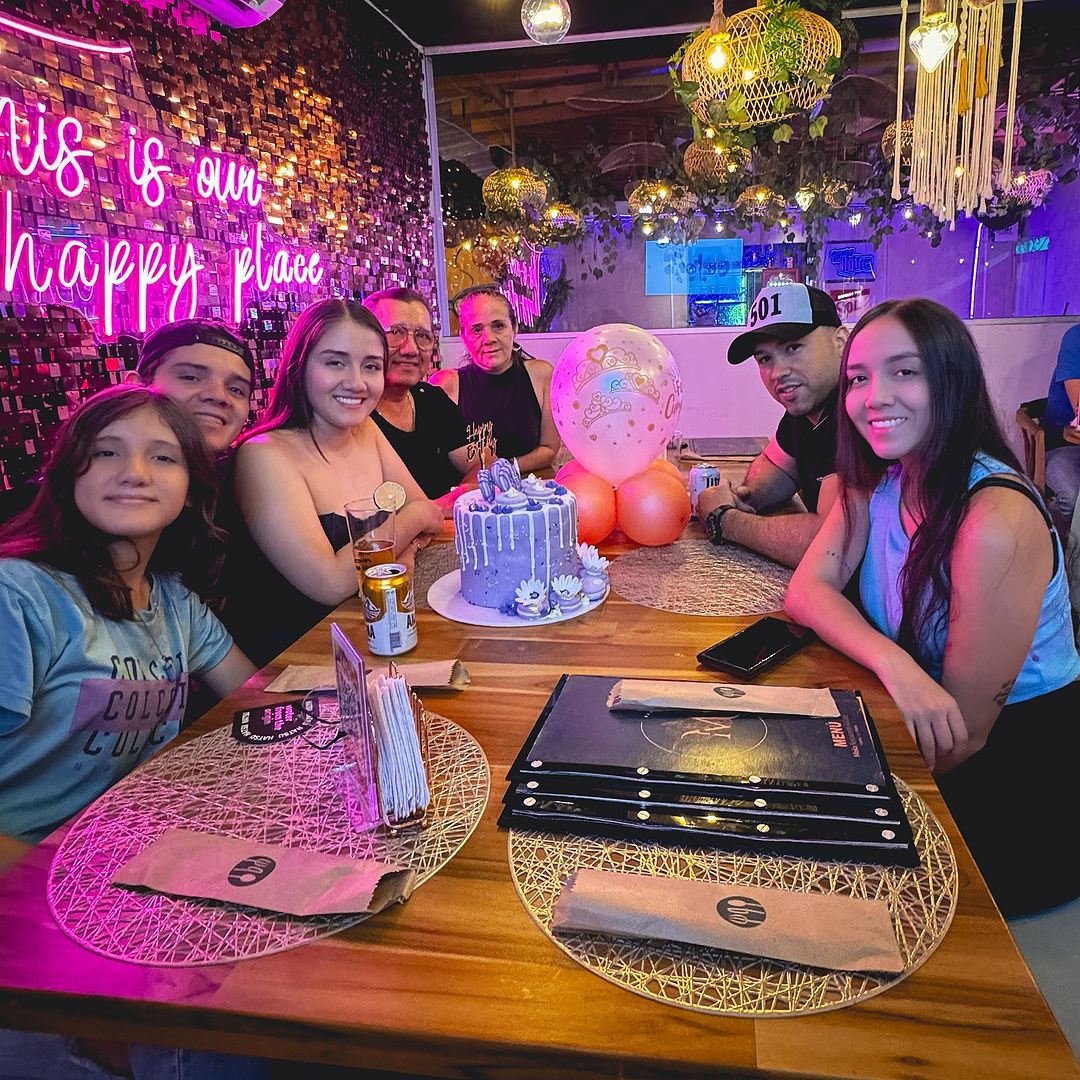 Gastrobar con personas compartiendo pastel de cumpleaños letrero neón globos